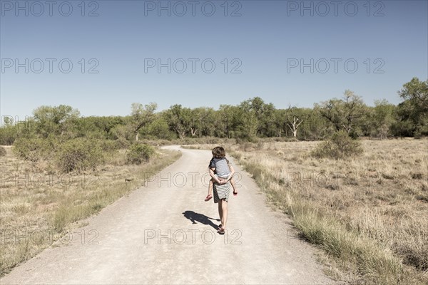 Caucasian girl carrying brother piggyback on dirt path