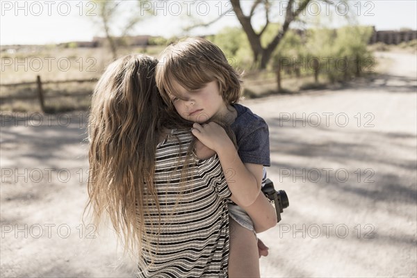 Caucasian girl carrying brother on dirt path