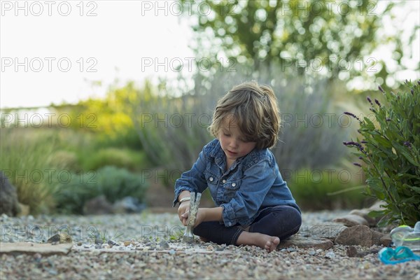 Caucasian boy sitting on ground smashing rocks with hammer