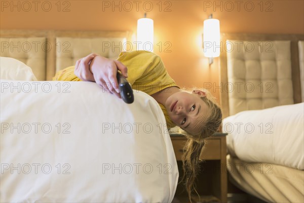Caucasian girl laying on bed in hotel room watching television