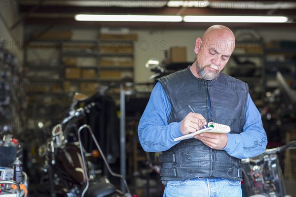 Caucasian man near motorcycle writing on notepad