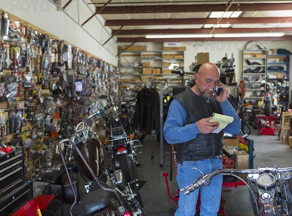 Caucasian man holding notepad near motorcycle talking on cell phone