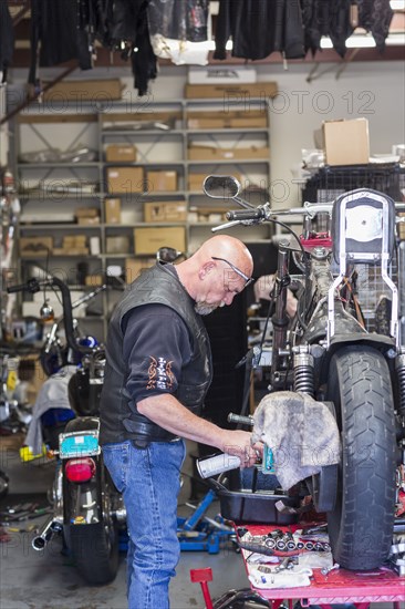 Caucasian man spraying lubricant on motorcycle