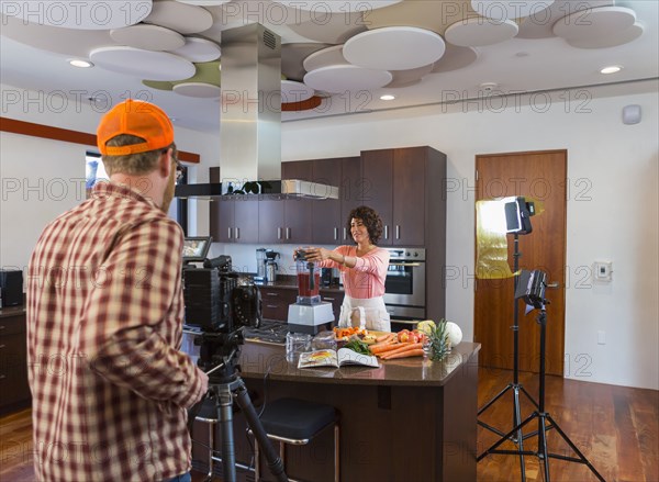 Cameraman recording woman preparing smoothie in domestic kitchen