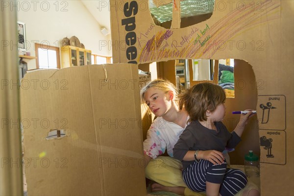 Caucasian boy and girl playing in cardboard house