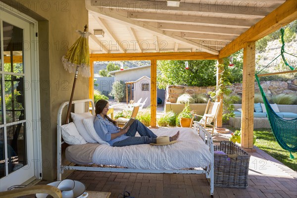 Older Caucasian woman reading books on bed on patio