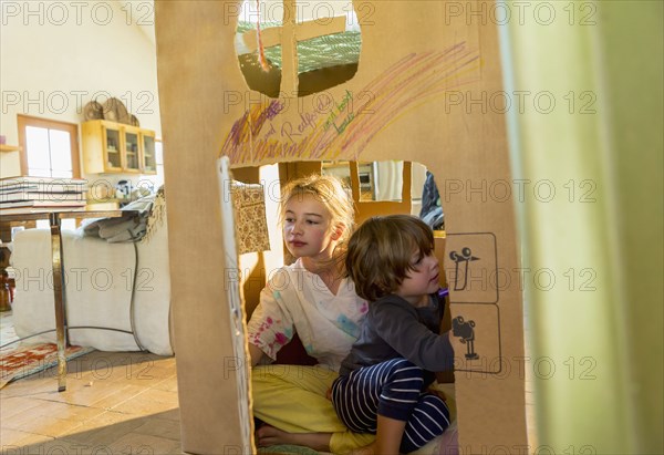 Caucasian boy and girl playing in cardboard house