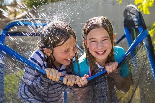 Water splashing on Caucasian girls leaning on netting