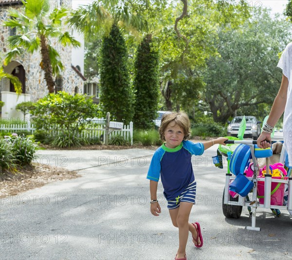 Caucasian boy pulling cart in street with mother