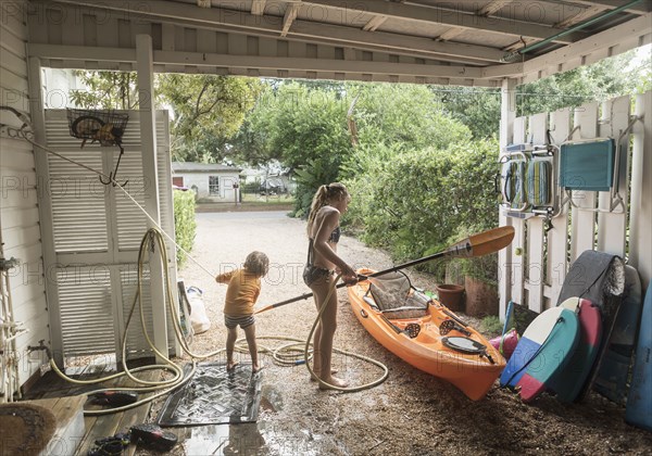 Caucasian brother and sister rinsing kayak with hose