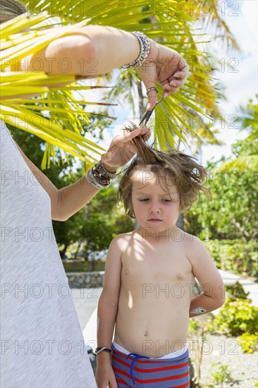 Caucasian mother cutting hair of son outdoors