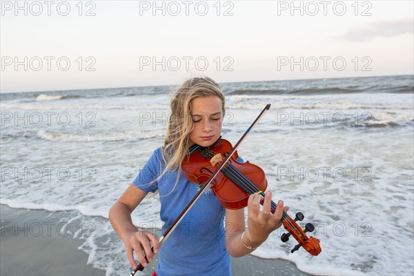 Caucasian girl playing violin at beach