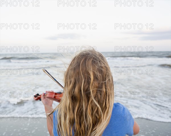 Rear view of Caucasian girl playing violin at beach