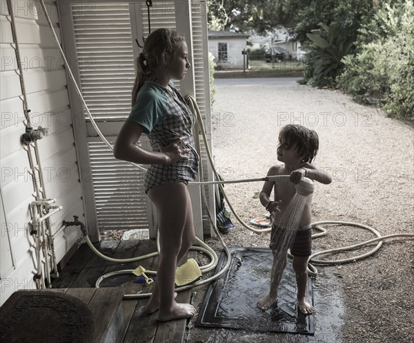 Frustrated Caucasian girl watching brother using shower outdoors