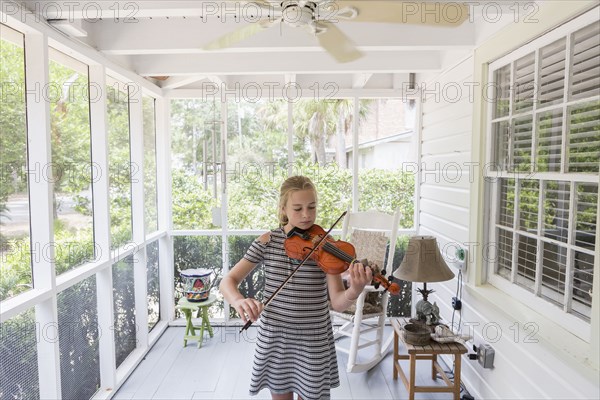 Caucasian girl playing violin on patio