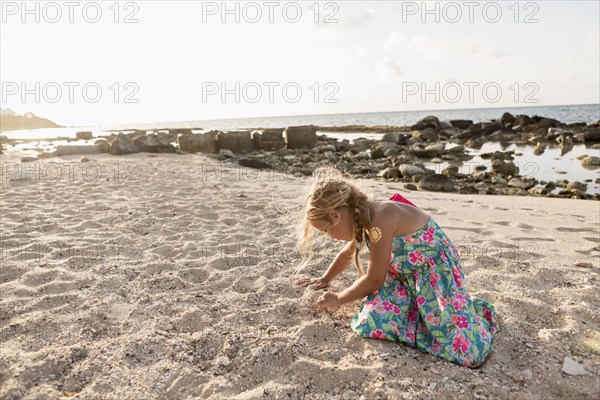 Caucasian girl playing in sand at beach