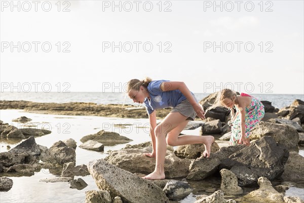 Caucasian girls walking on rocks at beach