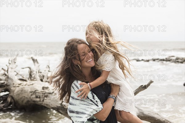 Caucasian mother hugging daughter near driftwood on beach