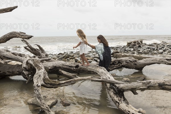 Caucasian mother and daughter walking on driftwood on beach