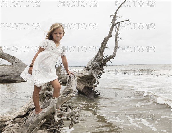 Caucasian girl posing on driftwood at beach