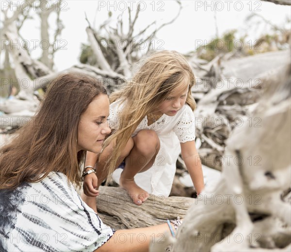 Caucasian mother and daughter examining driftwood on beach