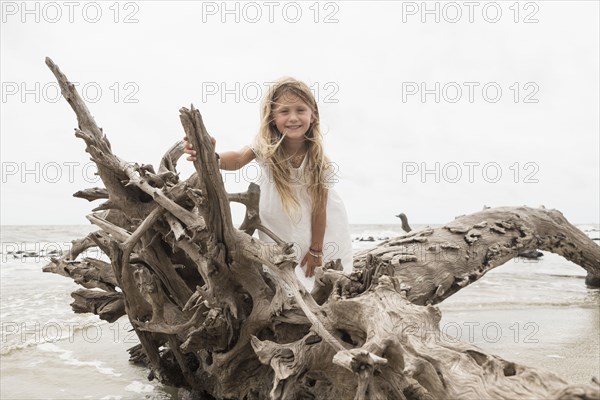 Caucasian girl posing on driftwood on beach