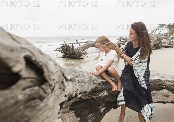 Caucasian mother and daughter sitting on driftwood on beach