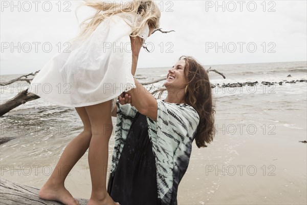 Caucasian mother and daughter playing on driftwood on beach