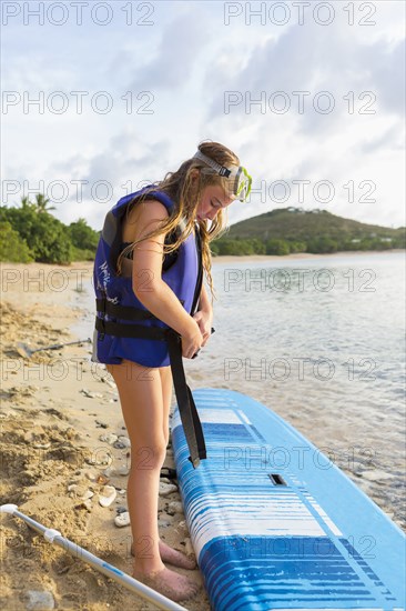 Caucasian girl fastening life jacket near paddleboard