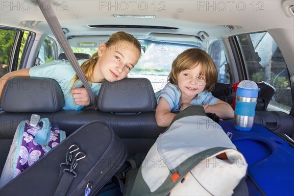 Caucasian brother and sister in car with luggage