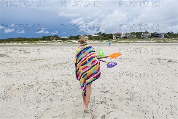 Caucasian girl walking on beach carrying net and shovels