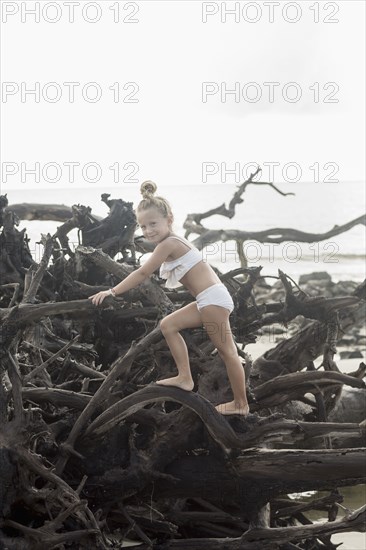 Caucasian girl climbing on driftwood at beach
