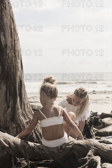 Caucasian girl sitting on driftwood at beach