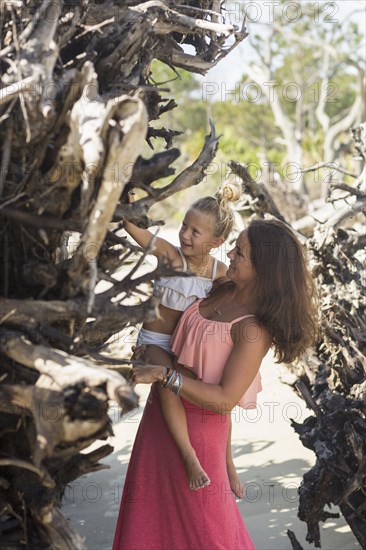 Caucasian mother and daughter examining driftwood at beach