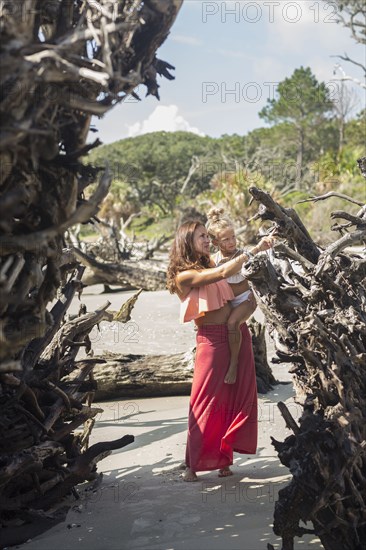 Caucasian mother and daughter examining driftwood on beach