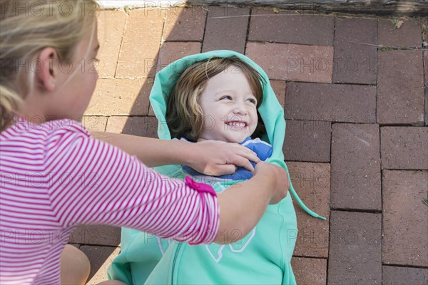 Caucasian girl talking brother into sweatshirt