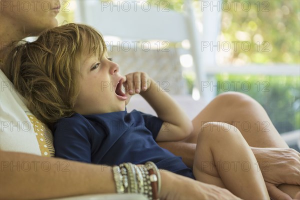 Caucasian boy yawning in the lap of mother