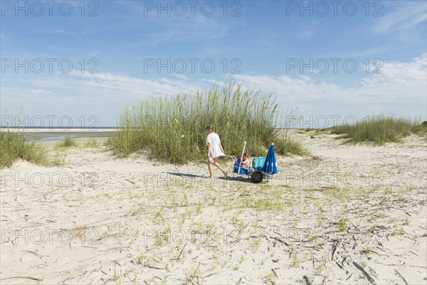 Caucasian mother pulling son in cart on the beach