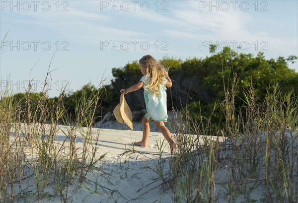 Caucasian girl walking on beach holding hat