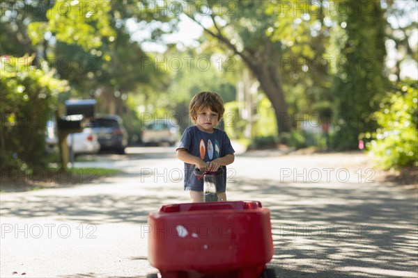 Caucasian boy pulling red wagon in street