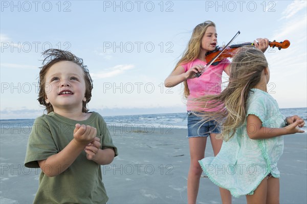 Caucasian girl playing violin on windy beach near brother and sister