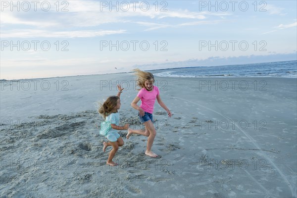 Caucasian sisters running on windy beach