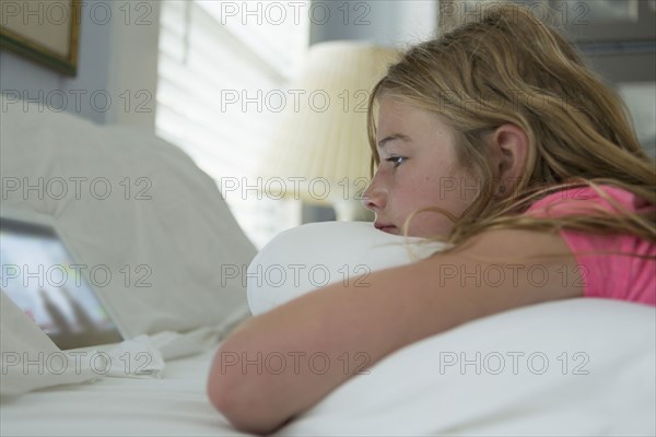 Caucasian girl laying on bed watching digital tablet
