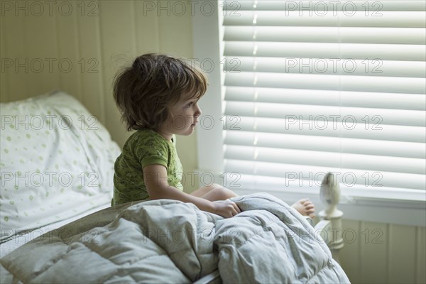 Caucasian boy sitting on bed near window