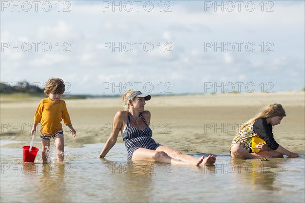 Caucasian families sitting in waves on the beach