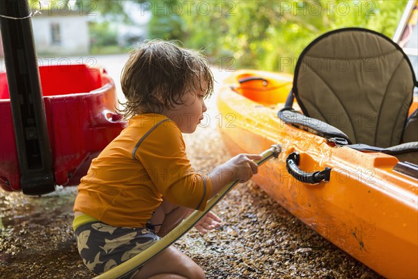 Caucasian boy washing kayak with hose