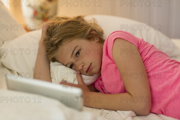 Caucasian girl laying on bed watching digital tablet