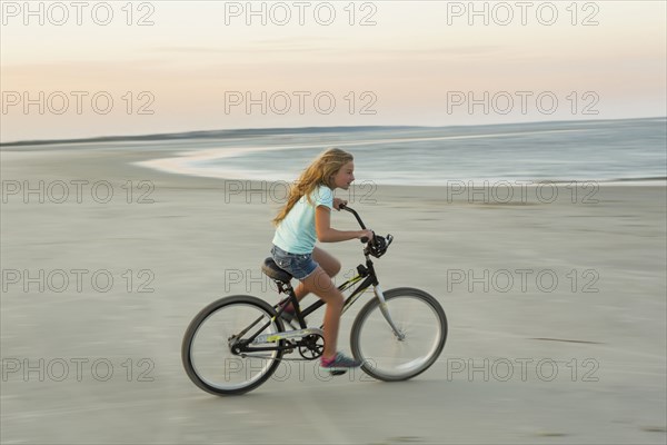 Caucasian girl riding bicycle on beach