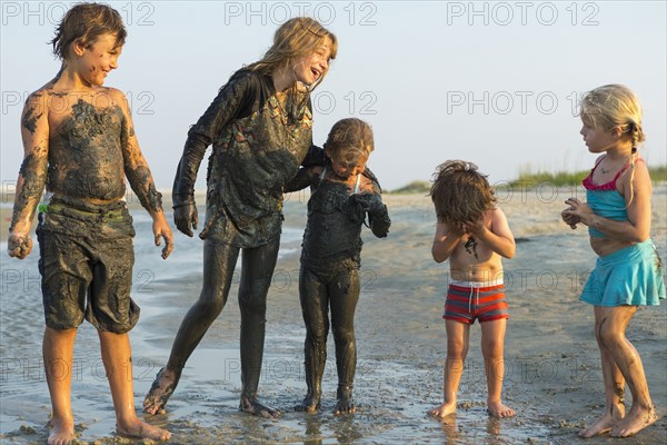 Caucasian brothers and sisters covered in mud playing on beach