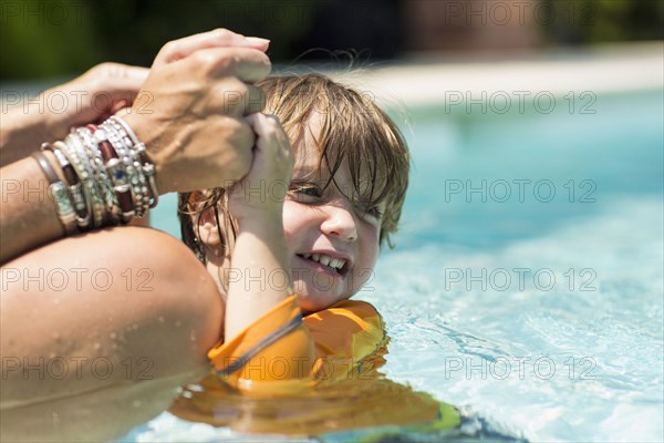 Caucasian mother holding hands of swimming boy